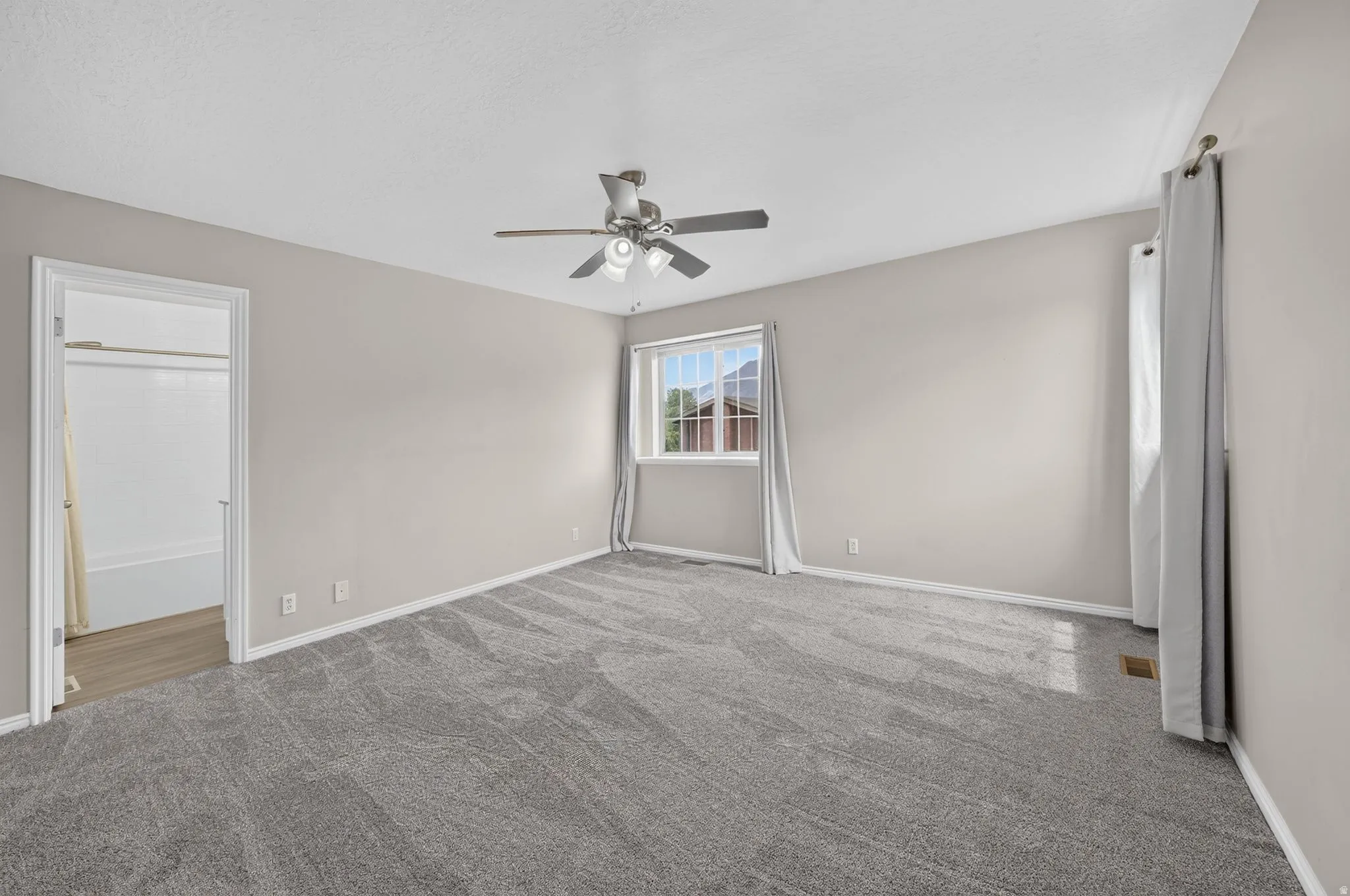 Spacious interior room featuring gray patterned carpet, light neutral wall tones, and a ceiling fan with integrated lighting