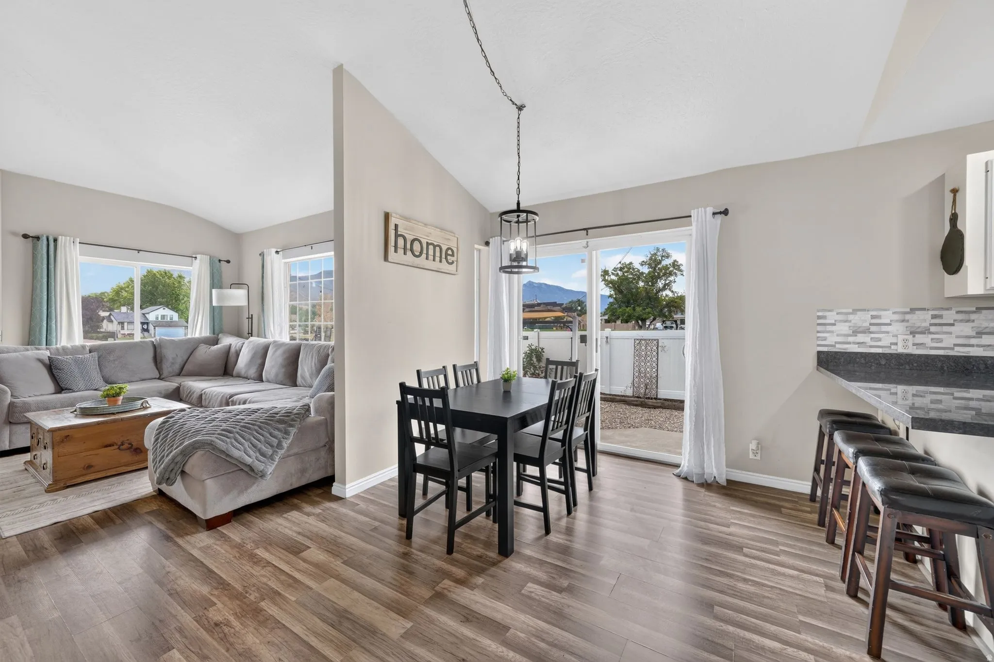 Open concept living and dining areas featuring wood-finish flooring, a kitchen counter with a tile backsplash, and a sliding glass door opening to an outdoor space