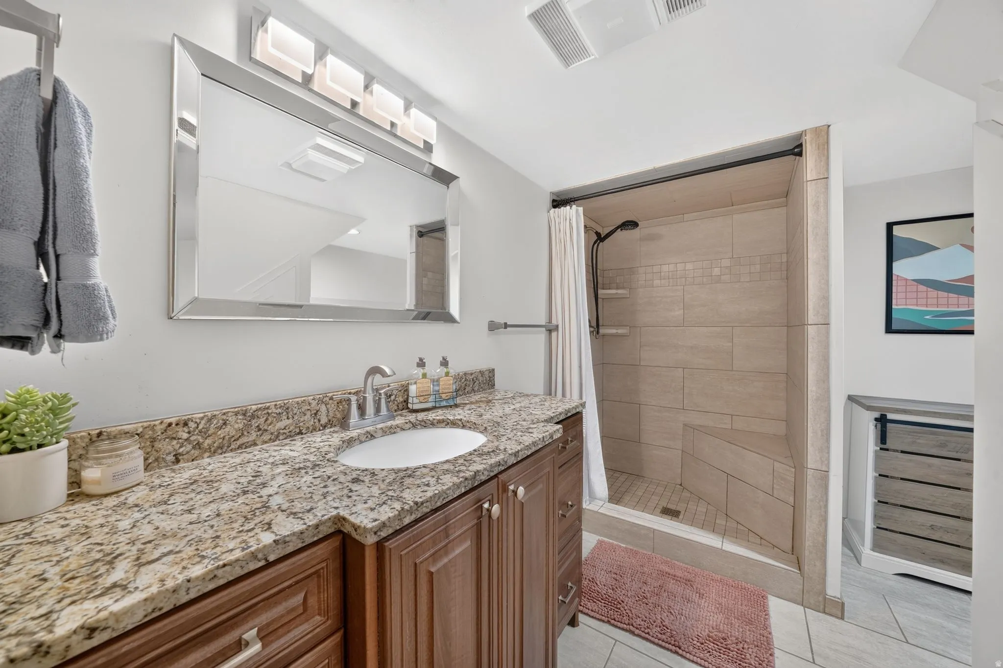 Bathroom featuring a wood-finish vanity with a granite countertop, undermount sink, and a framed mirror