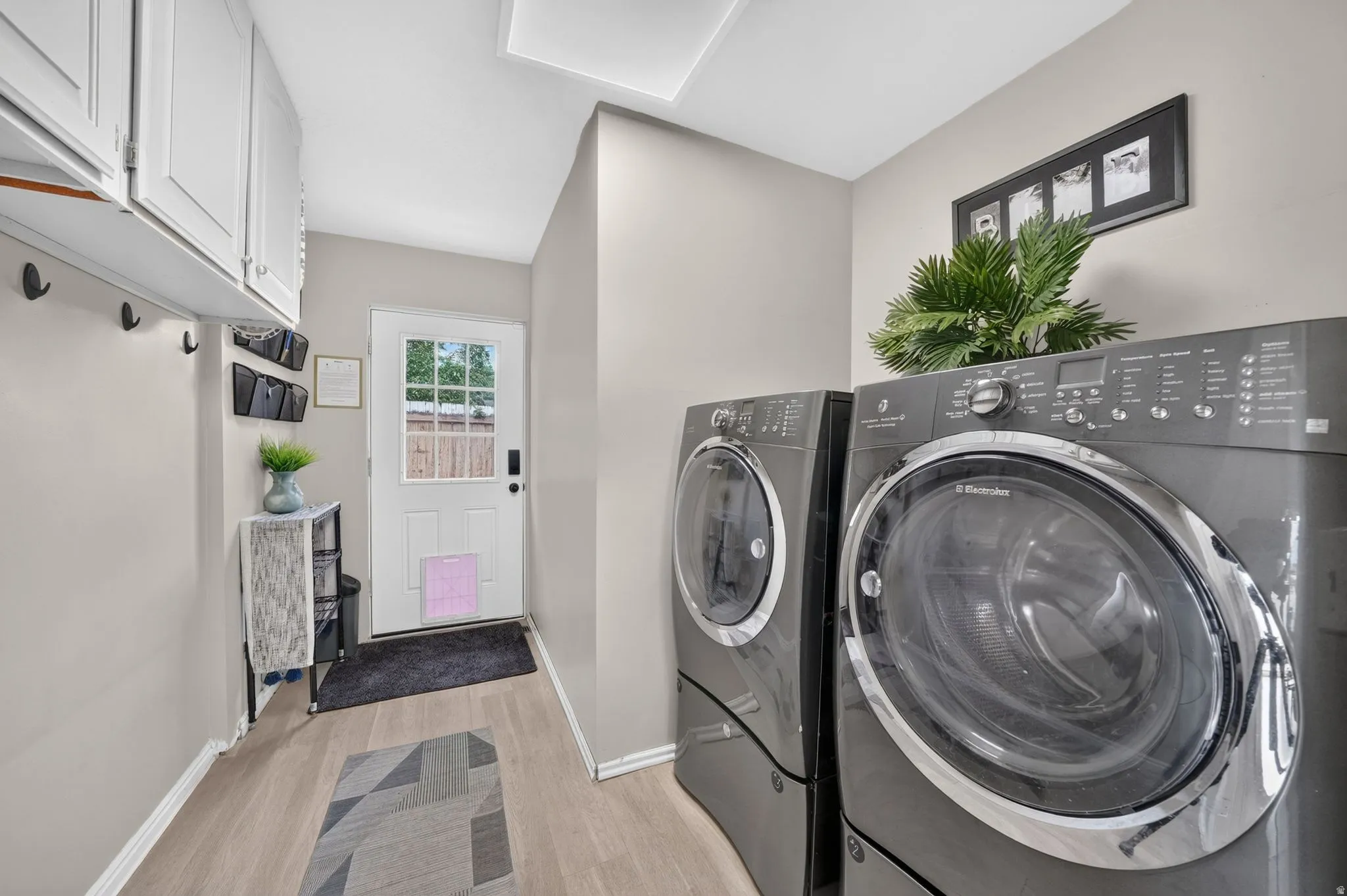 Laundry area featuring wood-finish flooring, white cabinetry, integrated coat hooks, and a paneled exterior door with window
