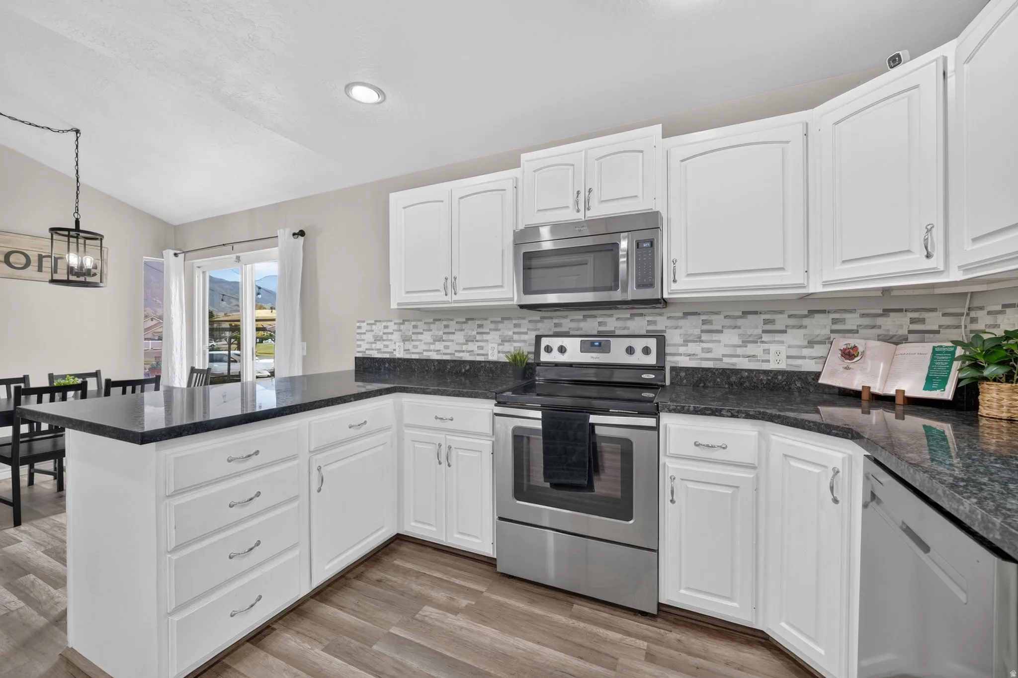Kitchen featuring white cabinetry, dark countertops, mosaic tile backsplash, stainless steel appliances, and wood-finish flooring