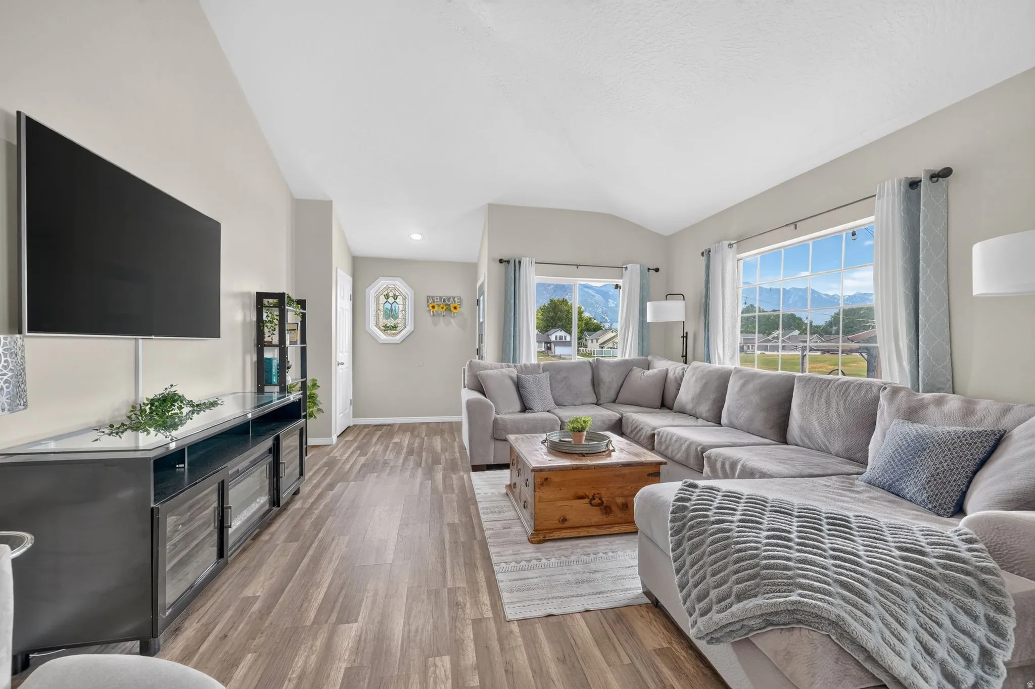 Expansive living area with wood-finish flooring, vaulted ceilings, and large windows