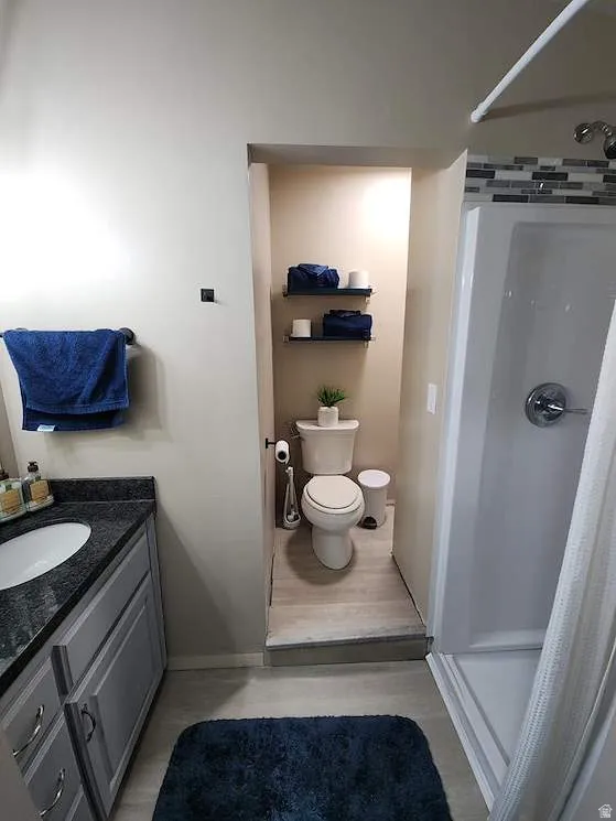 Bathroom featuring a single vanity with a dark countertop and undermount sink, light gray cabinetry, and a shower with a decorative tile accent band