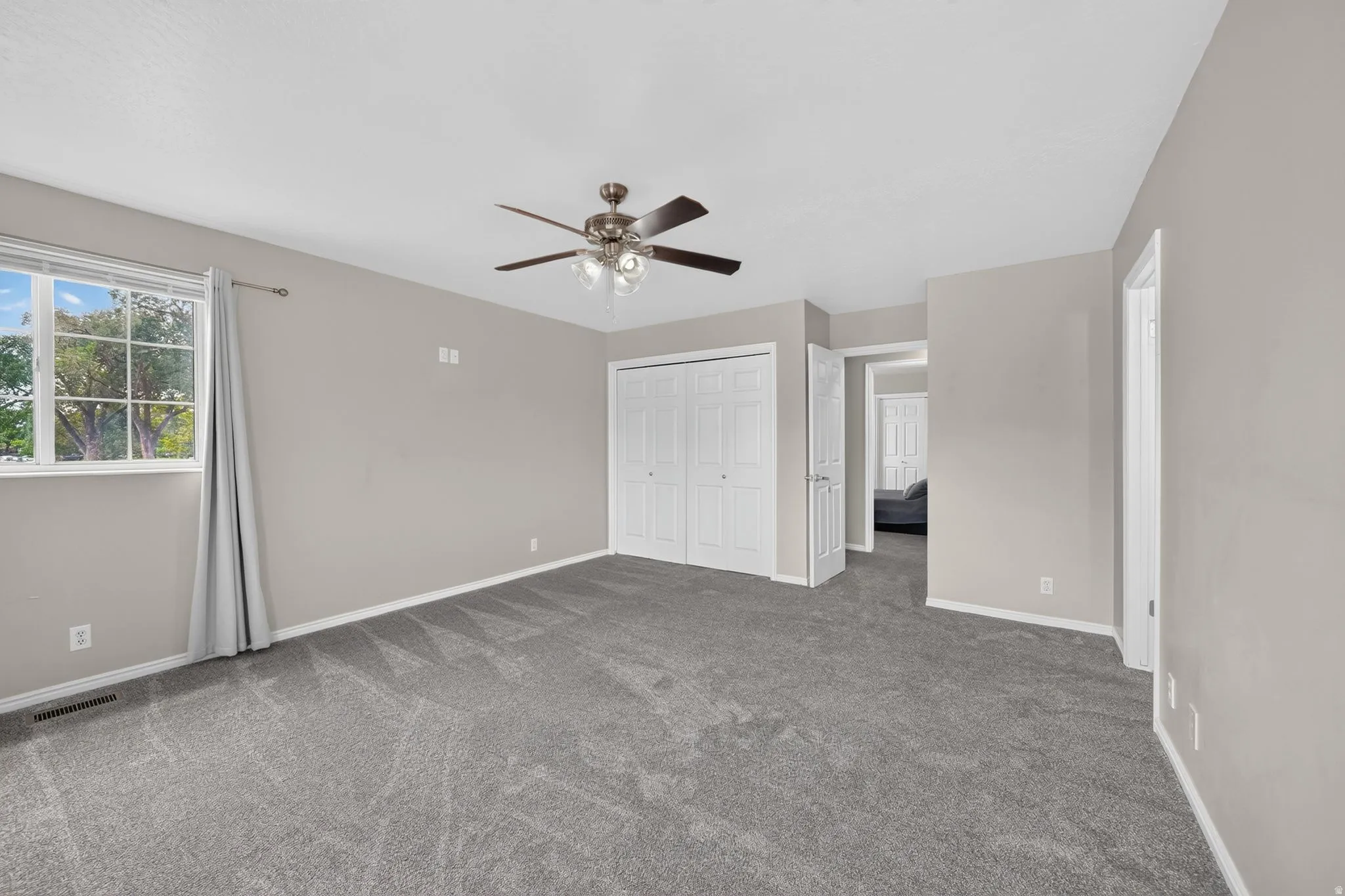 Carpeted room featuring a ceiling fan with integrated lighting, a large window with white trim, and a bi-fold closet door