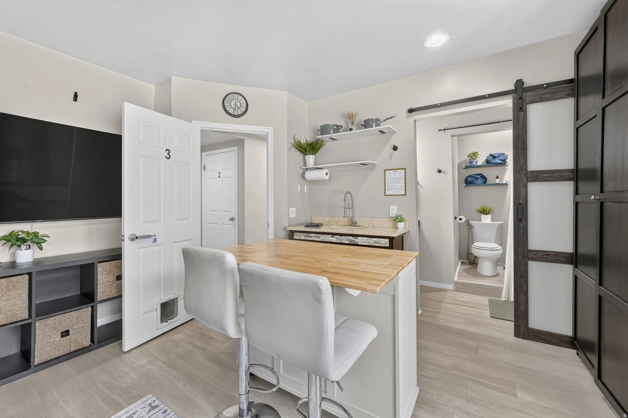 Compact kitchen area featuring a wood-finish countertop island with seating, a built-in sink with stone-look countertop, and overhead shelving