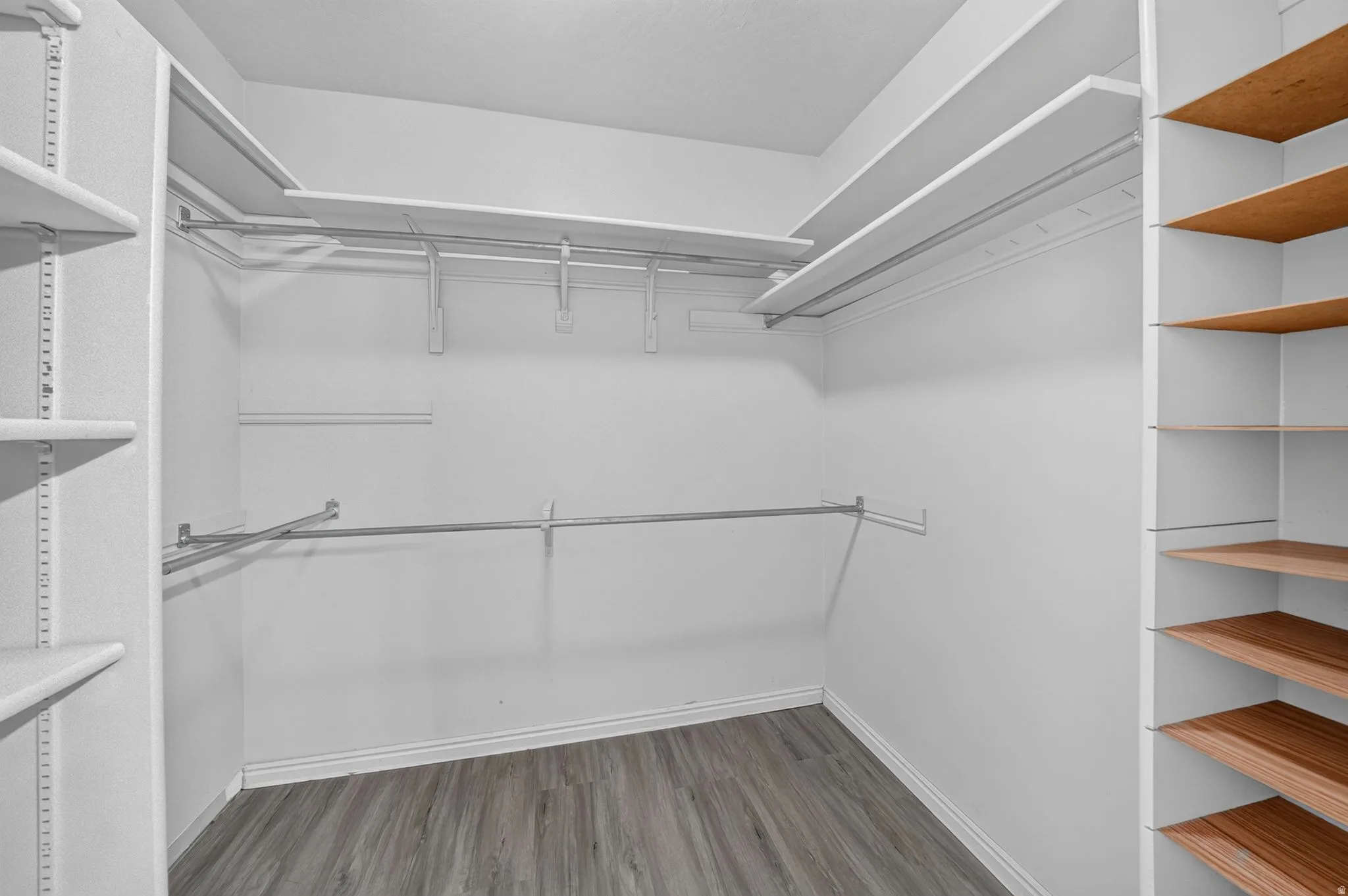 Walk-in closet featuring wood-finish flooring, white baseboards, multiple hanging rods, white shelving, and additional wood-toned shelving