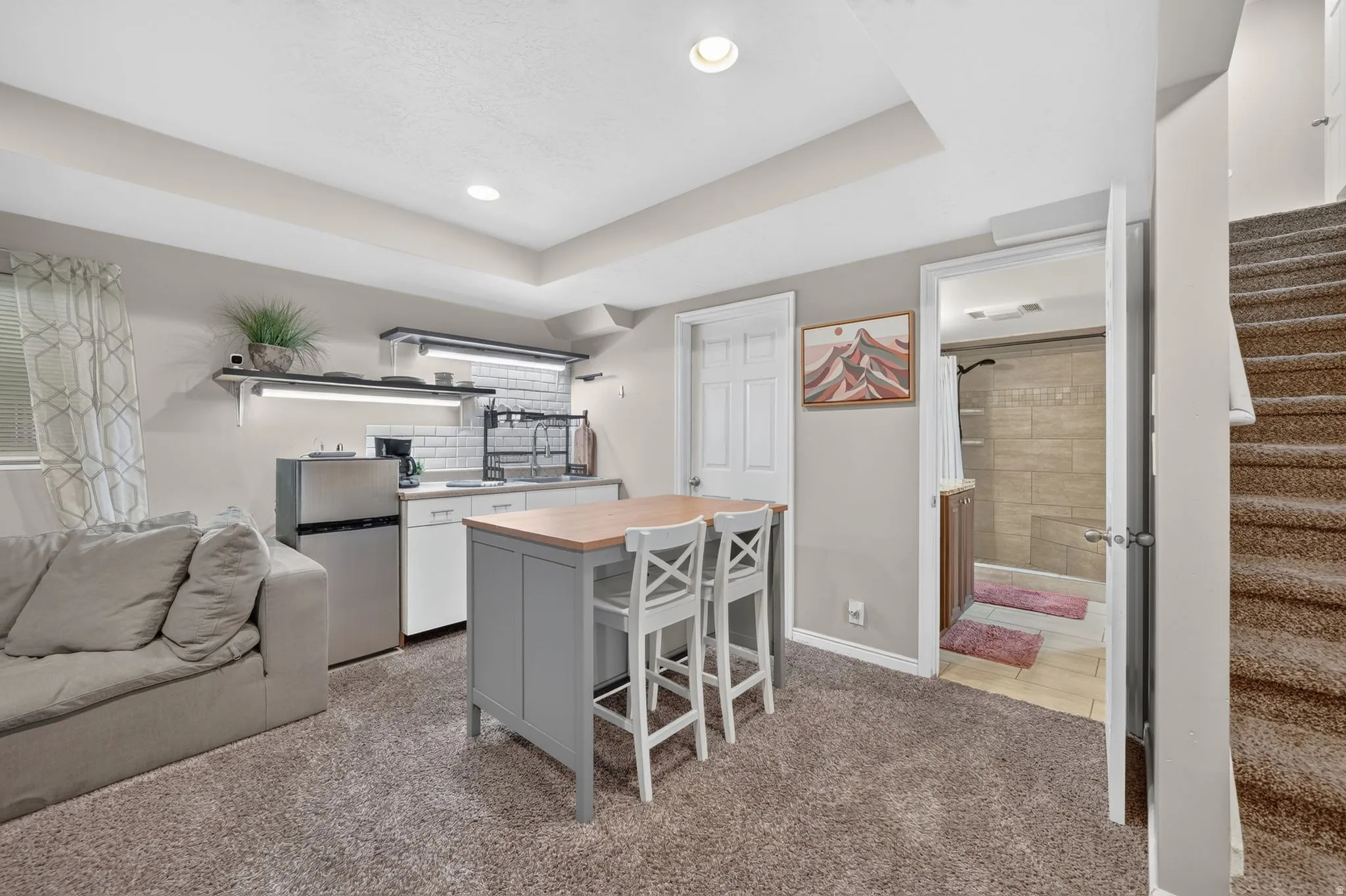 Carpeted living area featuring a compact kitchenette with a white subway tile backsplash and stainless steel sink