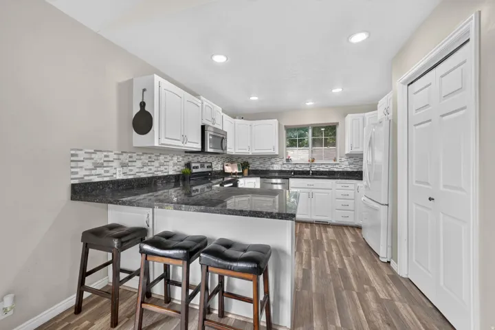 Kitchen featuring wood-finish flooring, white cabinetry, a dark countertop, a mosaic tile backsplash, and recessed lighting