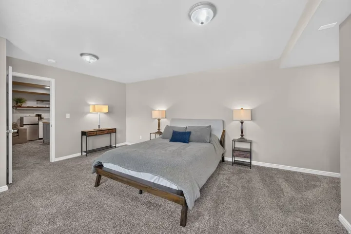 Spacious carpeted room featuring a neutral color palette, recessed ceiling light fixtures, and a doorway opening to an additional living space with built-in shelving