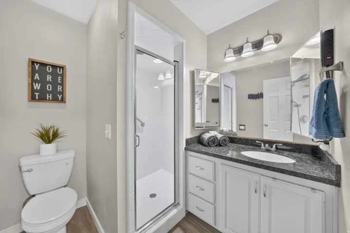 Modern bathroom featuring a glass-enclosed shower with subway tile, a vanity with a dark speckled countertop, white cabinetry, and wood-finish flooring