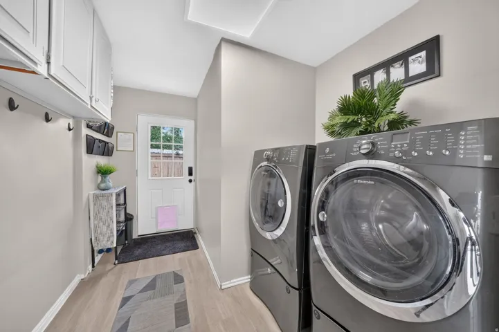 Laundry area featuring wood-finish flooring, white cabinetry, integrated coat hooks, and a paneled exterior door with window