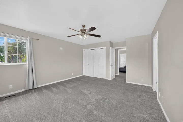 Carpeted room featuring a ceiling fan with integrated lighting, a large window with white trim, and a bi-fold closet door