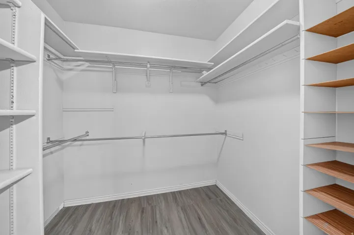 Walk-in closet featuring wood-finish flooring, white baseboards, multiple hanging rods, white shelving, and additional wood-toned shelving