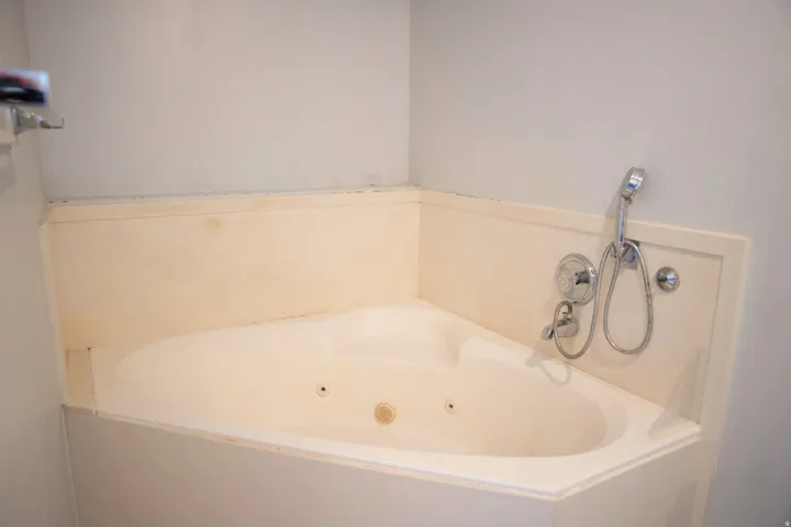 Corner jetted tub with chrome fixtures and an integrated handheld showerhead