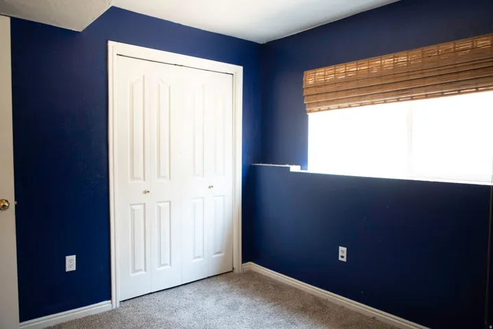Bedroom featuring a bi-fold closet, broad window with woven wood blinds, and textured wall finish