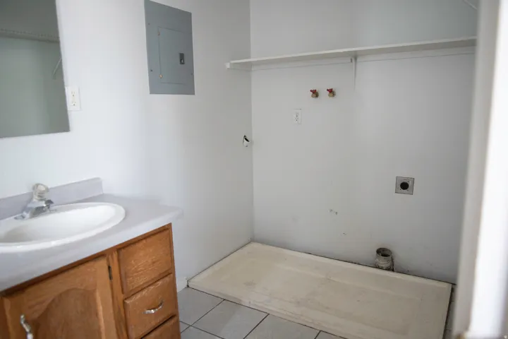Laundry area featuring a utility sink, wood-finish vanity, wall-mounted shelving, electrical panel, and tile flooring