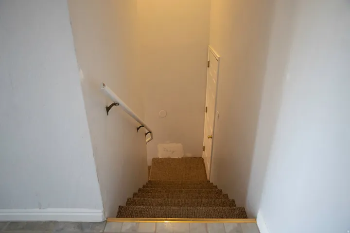 Stairwell featuring carpeted steps, a white handrail with dark brackets, and a white interior door at the base