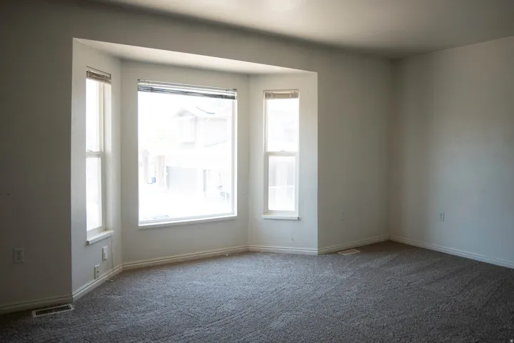 Spacious room featuring a prominent bay window with multiple panes, neutral wall color, grey carpet, and white baseboards
