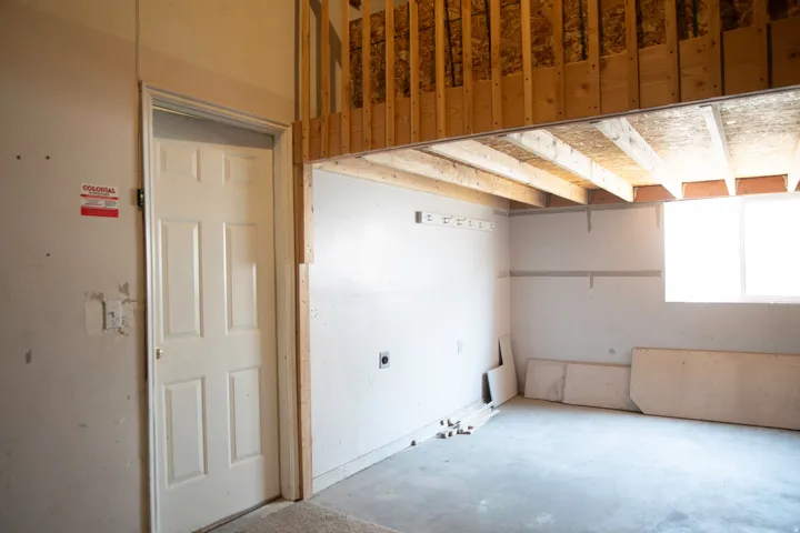 Unfinished interior space featuring a concrete floor, framed loft area, white paneled door, and a single window