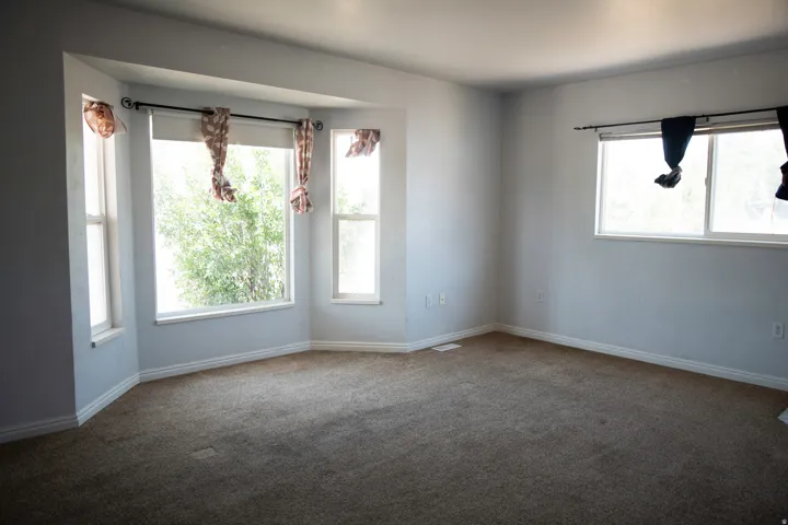 Spacious room featuring a bay window with multiple vertical windows, light gray wall paint, and brown carpet flooring