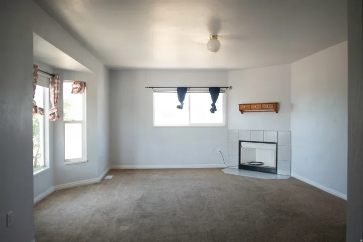 Living area featuring a corner fireplace with a tiled surround, a large bay window, and a secondary window