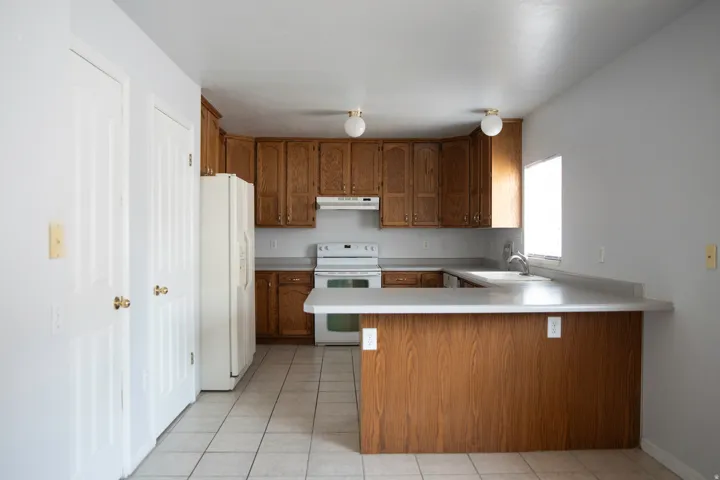 Kitchen featuring wood cabinetry, light-toned countertops, and a white appliance suite