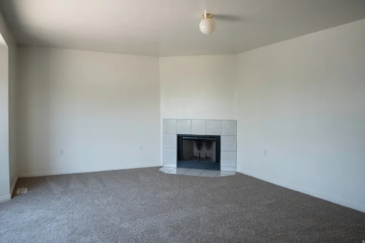 Carpeted room with a corner fireplace featuring white tile surround and hearth