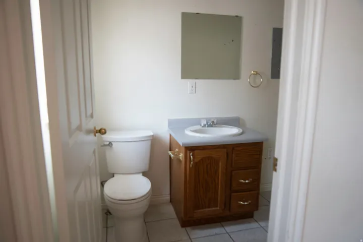 Bathroom featuring a white toilet, wood-finish vanity with a built-in sink, and square wall mirror