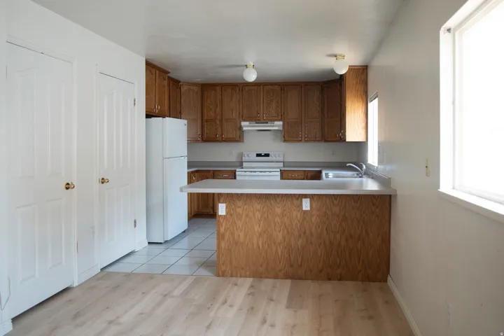 Kitchen featuring wood cabinetry, white appliances, light countertops, and a peninsula with a breakfast bar