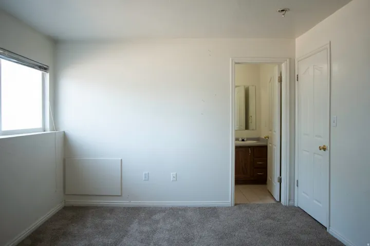 Carpeted room featuring a window with blinds, baseboard trim, and a panel heater