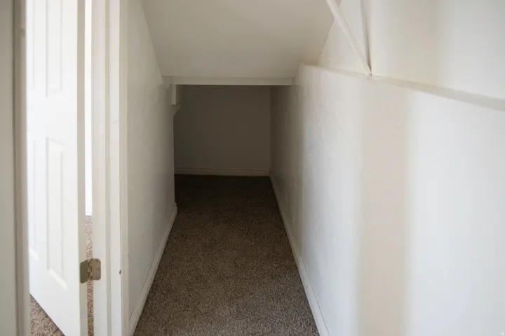Carpeted under-stair storage area with white painted walls and baseboards