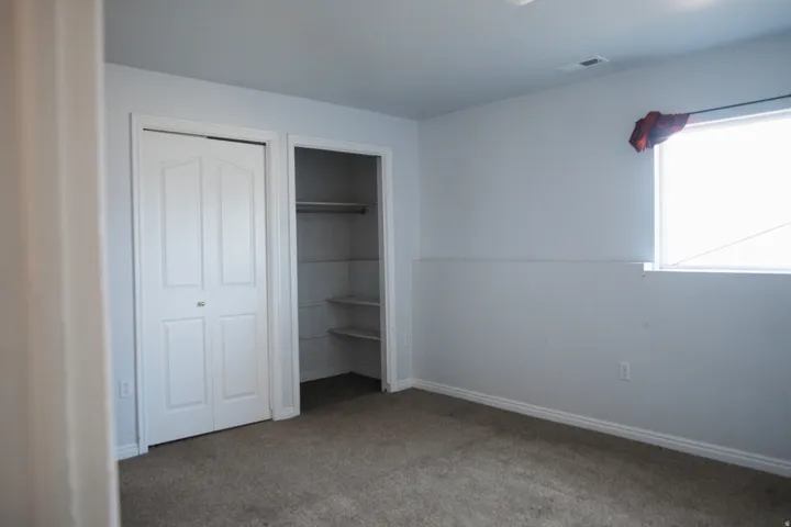 Carpeted room featuring a window, built-in shelving, two-panel bifold closet doors, and white baseboards