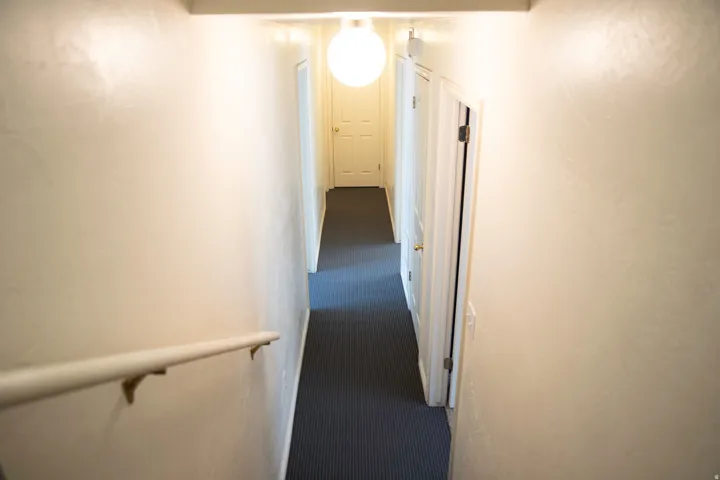 Hallway with blue carpet flooring, white walls, and a white ceiling-mounted globe light fixture