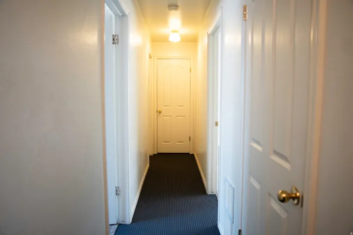 Interior hallway featuring white walls, white trim, and a dark patterned carpet