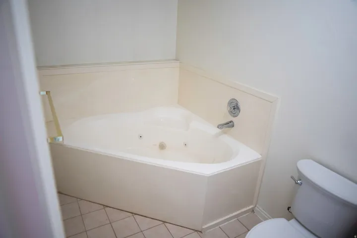 Corner soaking tub with jets, featuring a chrome faucet and light-toned tile flooring