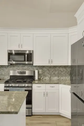 Modern kitchen featuring white shaker cabinetry, stainless steel appliances, herringbone tile backsplash, and light-toned countertops