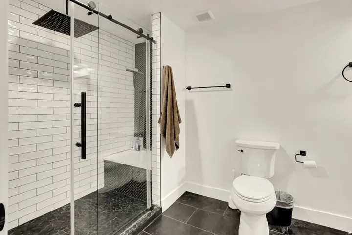 Spacious shower with clear glass enclosure and matte black hardware, featuring white subway tile walls, a built-in bench, and dark pebble floor