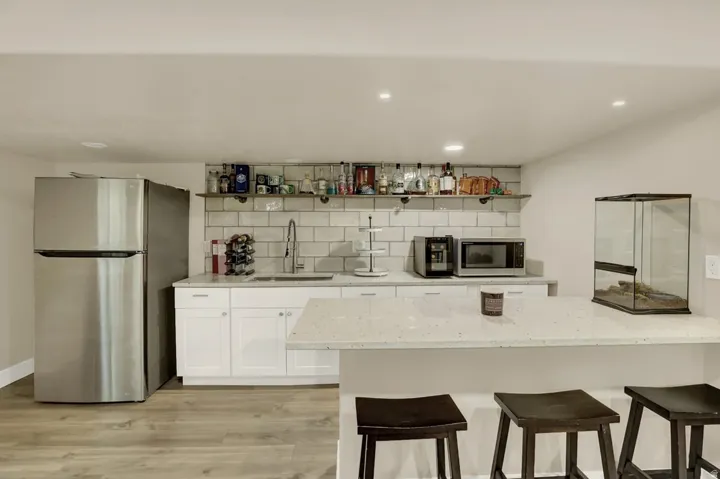 Kitchenette featuring a stainless steel refrigerator, white shaker-style cabinetry, a white subway tile backsplash, and a white countertop with an undermount sink