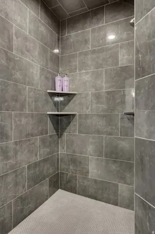 Shower stall featuring large format grey tile walls with white grout, a coordinating mosaic tile floor, recessed lighting, and built-in corner shelving