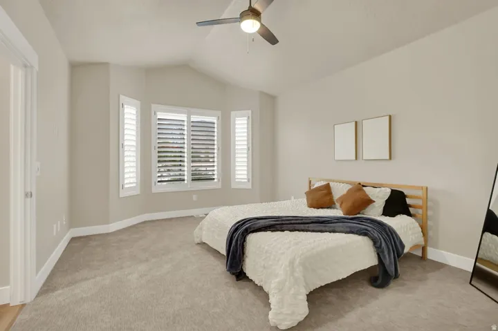 Carpeted room featuring a ceiling fan, vaulted ceiling, and bay windows with plantation shutters