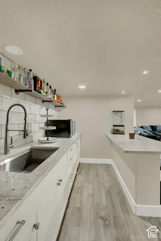 Wet bar featuring a stainless steel sink, granite-style countertop, white shaker-style cabinetry, subway tile backsplash, and open shelving