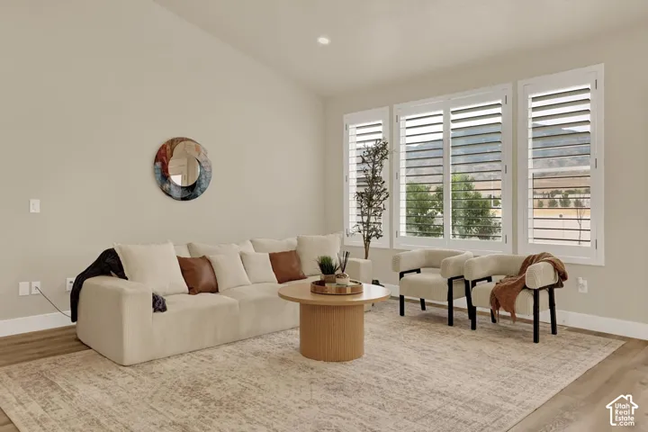 Spacious living area featuring vaulted ceilings, light neutral wall tones, and wood-finish flooring