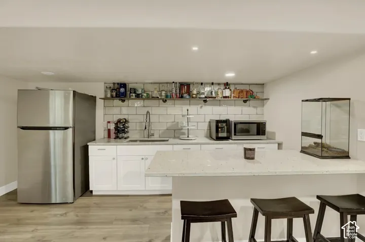 Kitchenette featuring a stainless steel refrigerator, white shaker-style cabinetry, a white subway tile backsplash, and a white countertop with an undermount sink