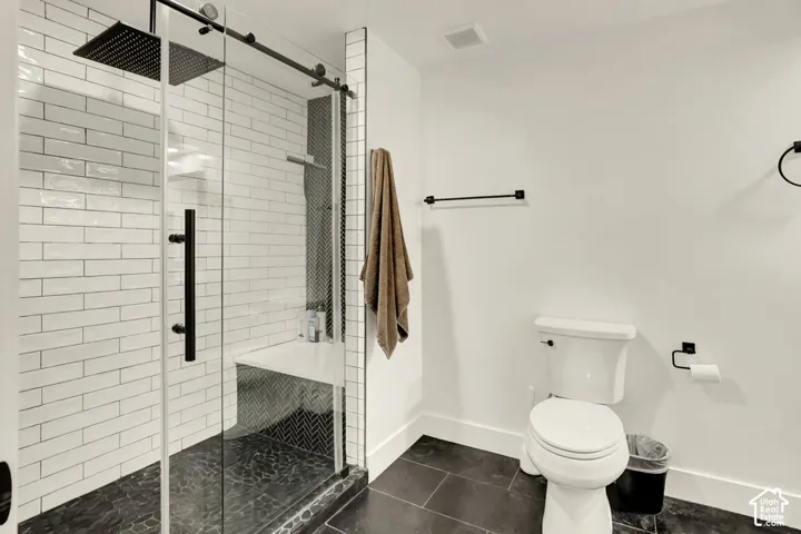 Spacious shower with clear glass enclosure and matte black hardware, featuring white subway tile walls, a built-in bench, and dark pebble floor