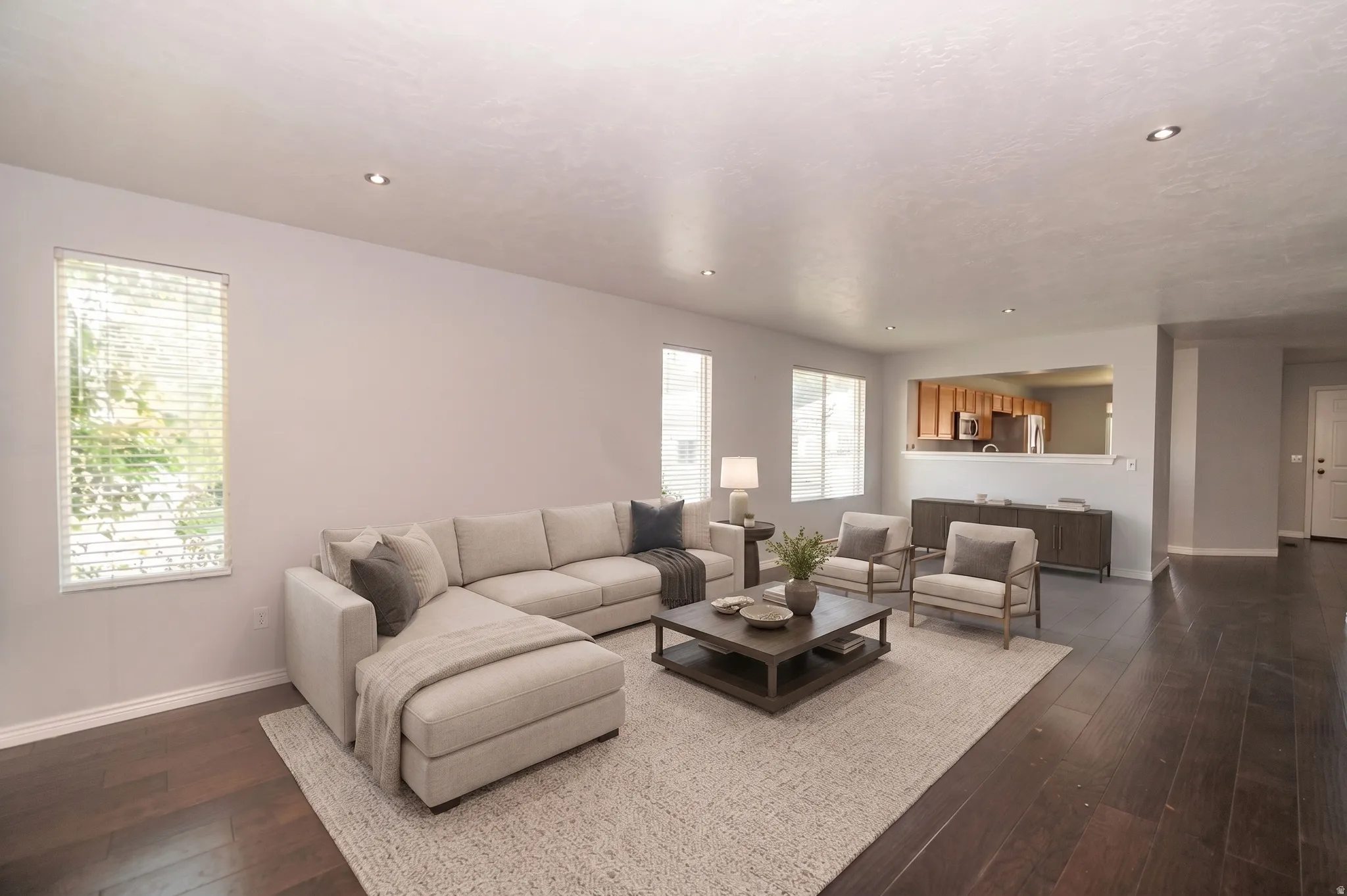 Recessed ceiling lighting, multiple windows, wood-finish flooring, and a kitchen pass-through