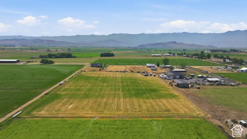 Expansive agricultural land featuring fields of varying crops, multiple outbuildings, and a mountainous backdrop
