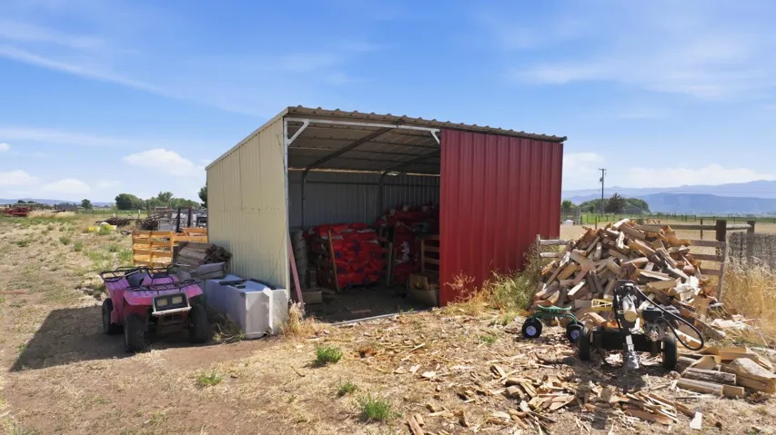 Open-sided metal shed featuring a galvanized roof and red and beige corrugated metal siding