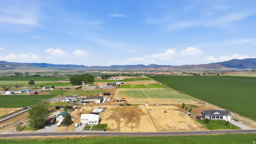 Expansive rural property featuring a large white residence with a dark roof and covered front porch, surrounded by agricultural fields and open land