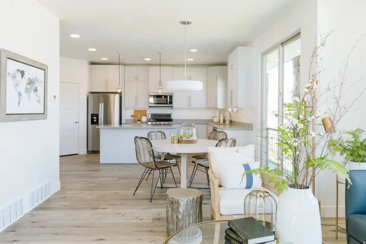 Open-concept kitchen and dining area featuring light wood-finish flooring, white cabinetry, stainless steel appliances, and a central island with countertop seating