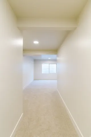 Recessed lighting illuminating a carpeted hallway leading to a room with a window featuring horizontal blinds